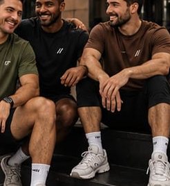 Três amigos sentados com camisetas oliva, preta e marrom